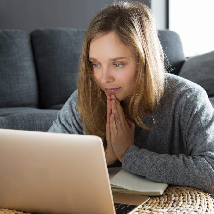 Positive girl having video call and asking for help. Young woman keeping hands together in pray and focusing on laptop monitor. Communication or asking concept