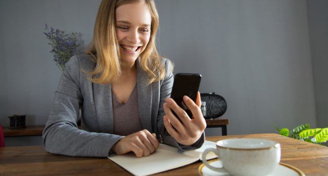 Happy girl in jacket overjoyed with video call. Young woman holding smartphone and smiling at screen. Communication or good news concept