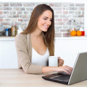 Portrait of beautiful young woman using her laptop in the kitchen.